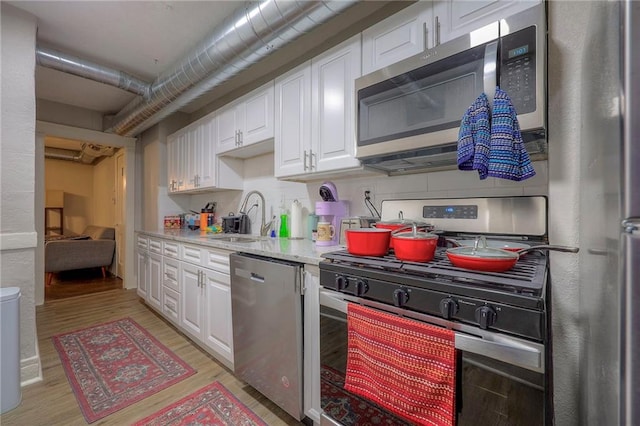 kitchen with stainless steel appliances, sink, white cabinets, and light wood-type flooring