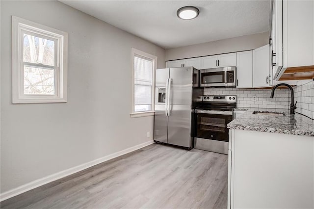 kitchen with appliances with stainless steel finishes, white cabinetry, sink, backsplash, and light stone counters