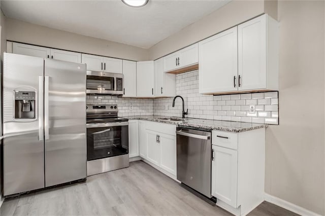 kitchen featuring sink, stone counters, white cabinetry, backsplash, and stainless steel appliances