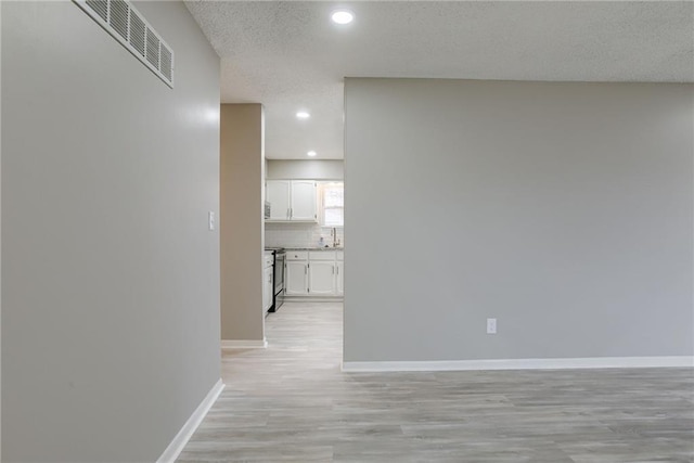 hallway with sink, a textured ceiling, and light hardwood / wood-style flooring