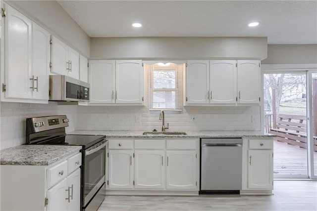 kitchen with light stone counters, appliances with stainless steel finishes, sink, and white cabinets