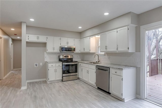 kitchen featuring appliances with stainless steel finishes, white cabinetry, sink, light stone countertops, and light wood-type flooring