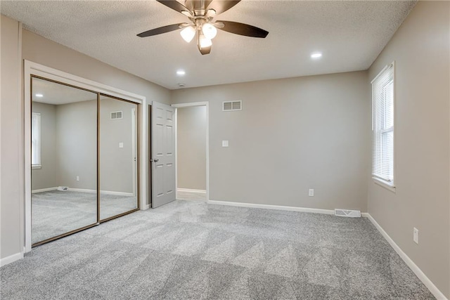 unfurnished bedroom featuring ceiling fan, a closet, light carpet, and a textured ceiling