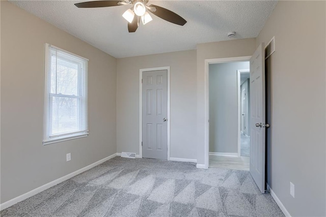 unfurnished bedroom with ceiling fan, light carpet, and a textured ceiling