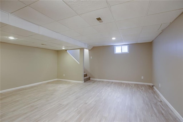 basement featuring a paneled ceiling and light hardwood / wood-style flooring