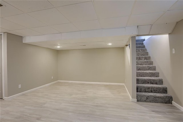 basement with a paneled ceiling and light wood-type flooring