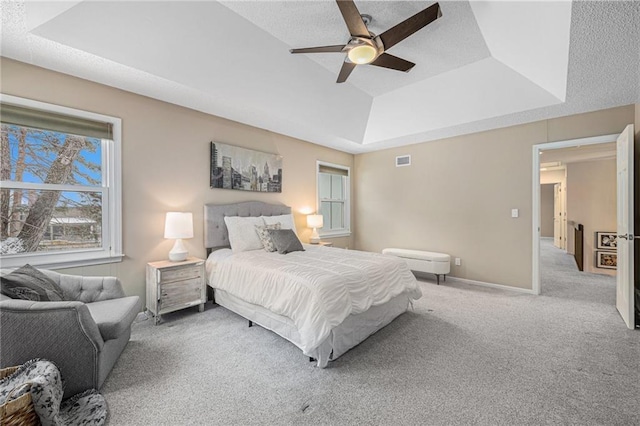 bedroom with a raised ceiling, light colored carpet, visible vents, ceiling fan, and baseboards