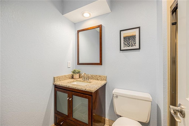 bathroom featuring toilet, a textured wall, and vanity