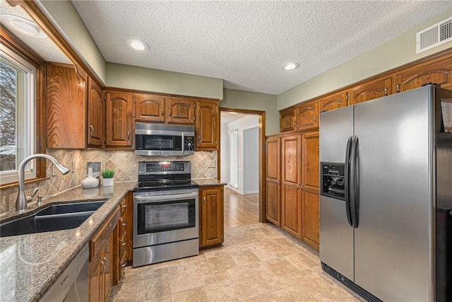 kitchen featuring visible vents, brown cabinets, stainless steel appliances, stone counters, and a sink