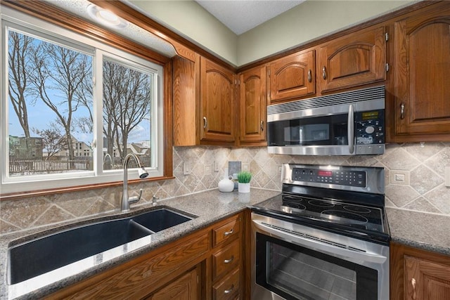 kitchen featuring stainless steel appliances, tasteful backsplash, a sink, and brown cabinets