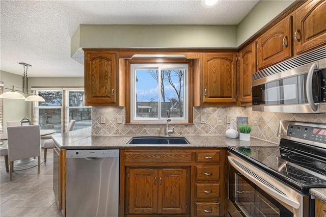 kitchen with appliances with stainless steel finishes, brown cabinetry, a sink, and decorative light fixtures