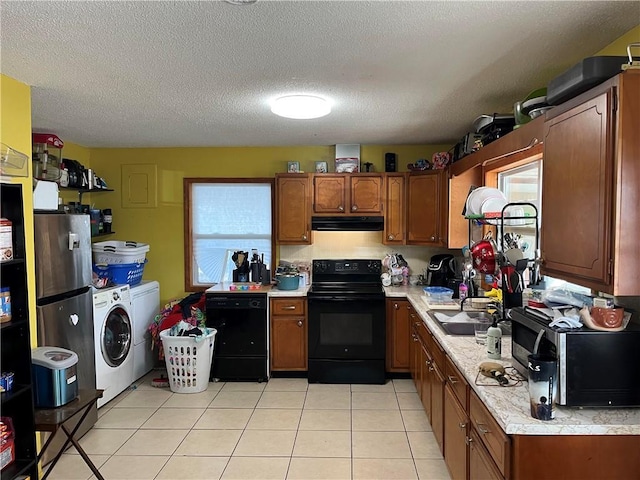 kitchen featuring light tile patterned flooring, range hood, washer / dryer, sink, and black appliances