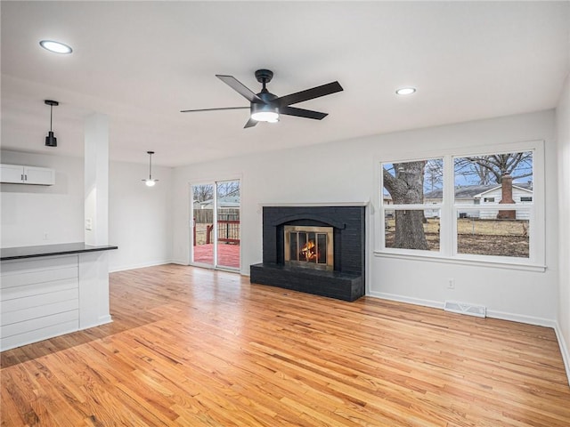 unfurnished living room with ceiling fan, a brick fireplace, and light wood-type flooring