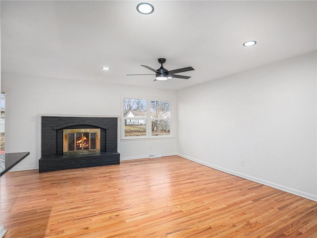 unfurnished living room featuring ceiling fan, a fireplace, and light wood-type flooring