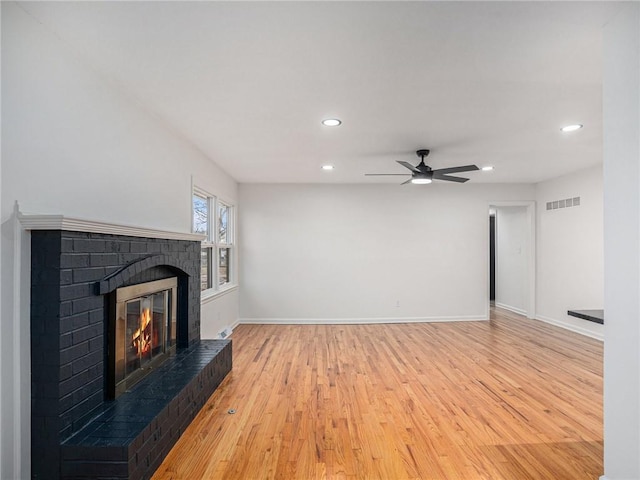 unfurnished living room with ceiling fan, a brick fireplace, and light wood-type flooring