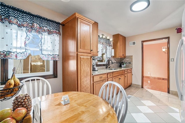 kitchen with sink, backsplash, fridge, light tile patterned floors, and light stone counters