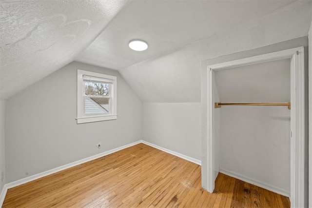 additional living space featuring wood-type flooring, a textured ceiling, and vaulted ceiling