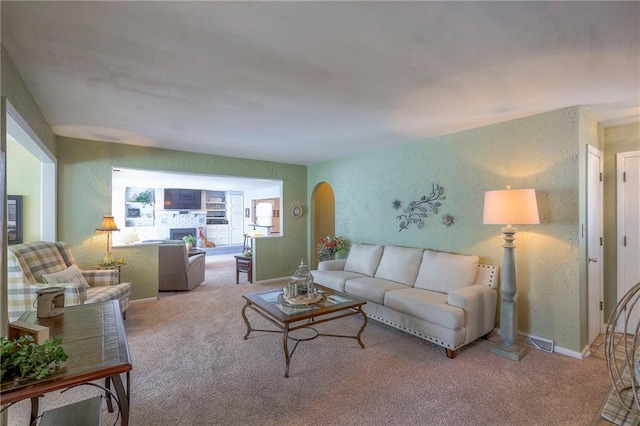 living area with light carpet, a fireplace, arched walkways, and a textured wall