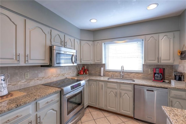 kitchen with light tile patterned floors, appliances with stainless steel finishes, a sink, and white cabinets