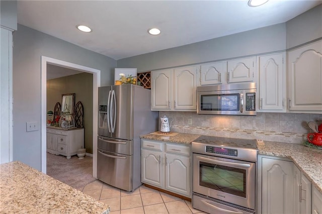 kitchen with stainless steel appliances, tasteful backsplash, white cabinetry, and light stone counters