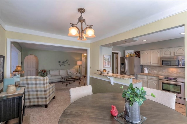 dining area with light carpet, arched walkways, and an inviting chandelier