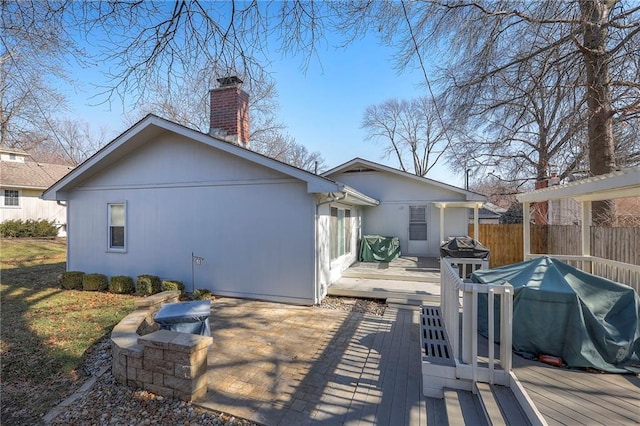 rear view of house with a chimney, a wooden deck, and fence