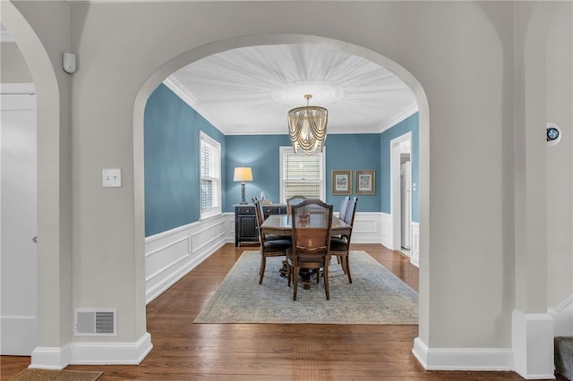 dining room featuring arched walkways, a wainscoted wall, a notable chandelier, visible vents, and dark wood-type flooring