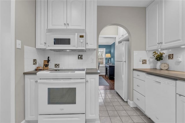 kitchen featuring arched walkways, light tile patterned flooring, white appliances, white cabinetry, and dark countertops