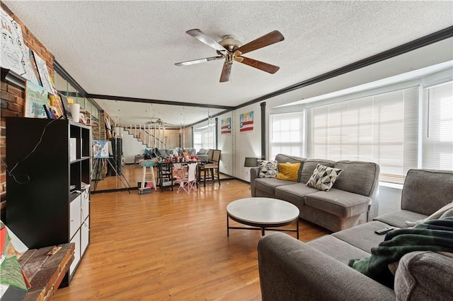 living area with a ceiling fan, crown molding, light wood finished floors, and stairs