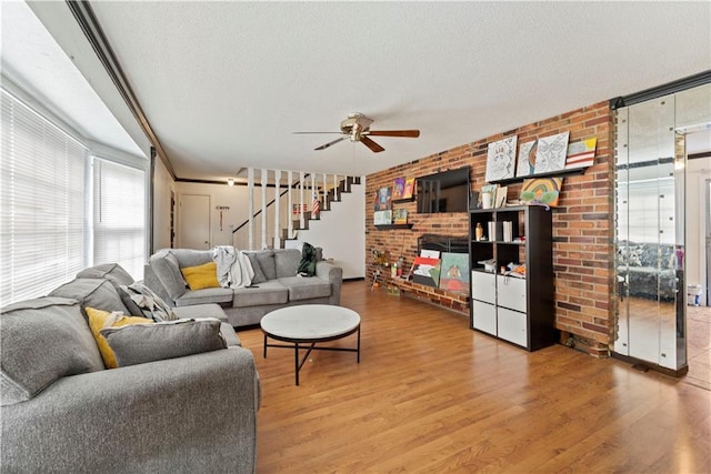 living area with a textured ceiling, brick wall, wood finished floors, a ceiling fan, and stairway