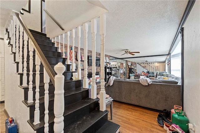 stairs featuring a textured wall, ceiling fan, a textured ceiling, and wood finished floors