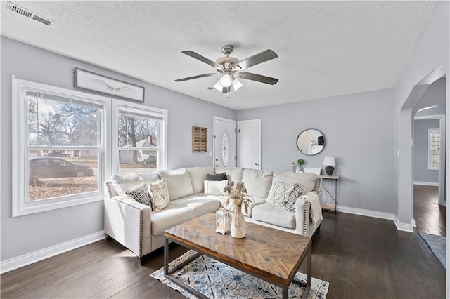 living room with arched walkways, dark wood finished floors, visible vents, and baseboards