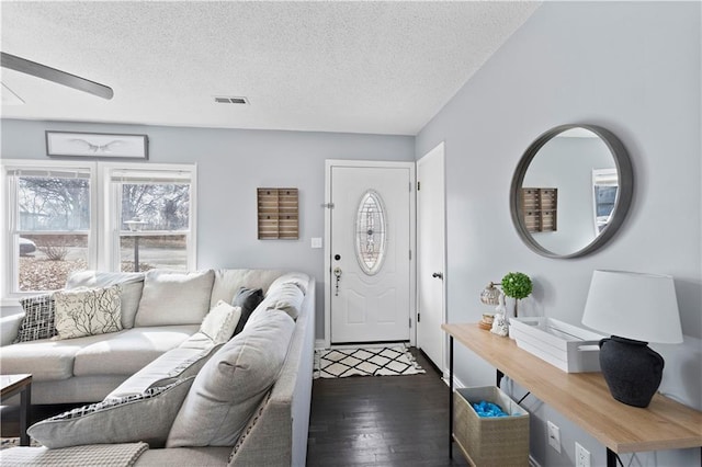 living room featuring a textured ceiling, ceiling fan, dark wood-style flooring, and visible vents