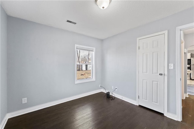 unfurnished room with arched walkways, dark wood-type flooring, visible vents, and baseboards