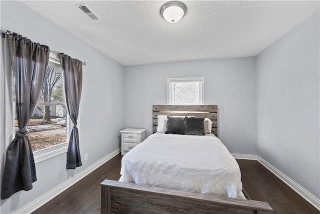 bedroom with visible vents, a textured ceiling, baseboards, and wood finished floors