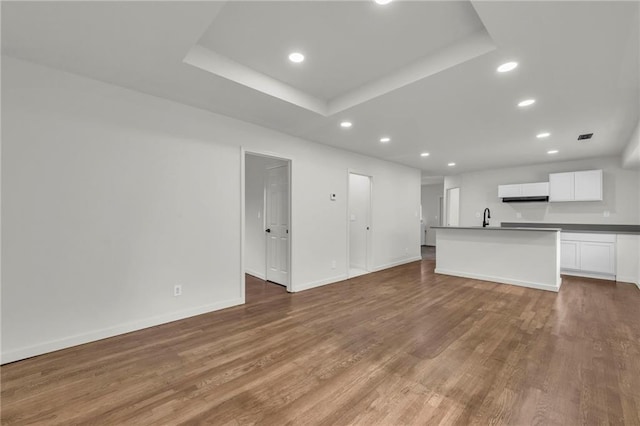 unfurnished living room featuring sink, hardwood / wood-style floors, and a tray ceiling