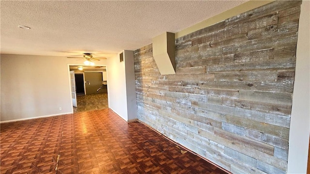 spare room featuring ceiling fan, parquet flooring, wooden walls, and a textured ceiling