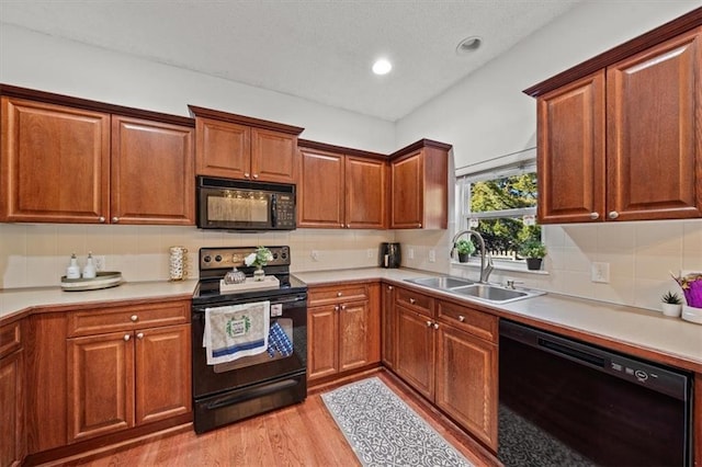 kitchen with tasteful backsplash, black appliances, light wood-type flooring, and a sink