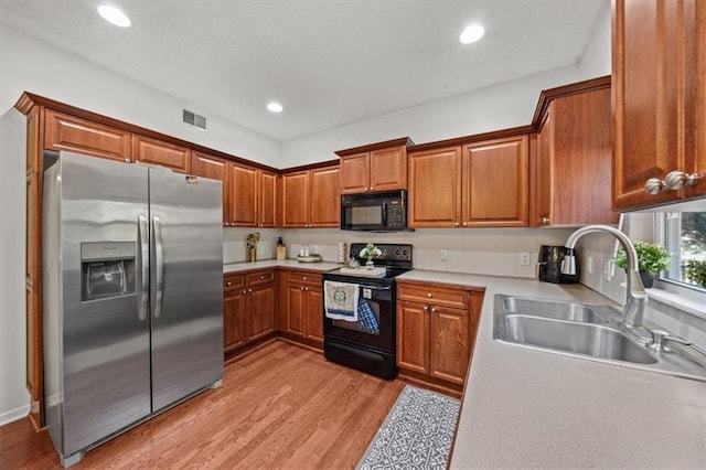 kitchen featuring light wood finished floors, visible vents, brown cabinets, black appliances, and a sink