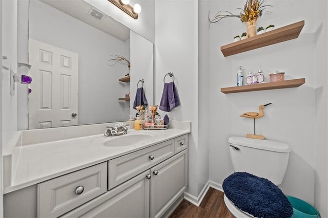 half bathroom with visible vents, baseboards, toilet, wood finished floors, and vanity