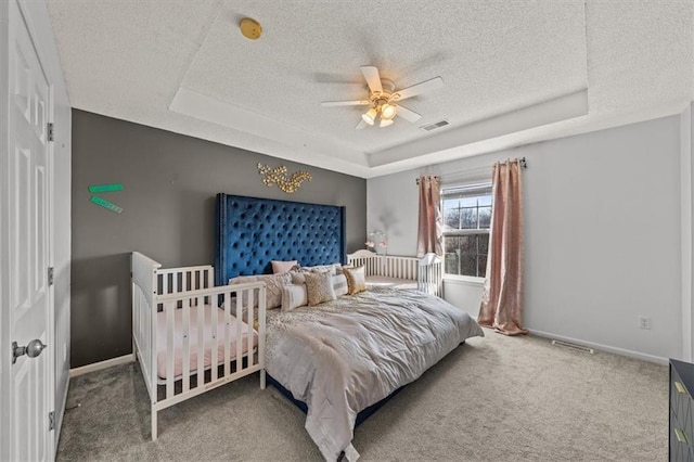 bedroom with carpet, a tray ceiling, baseboards, and visible vents