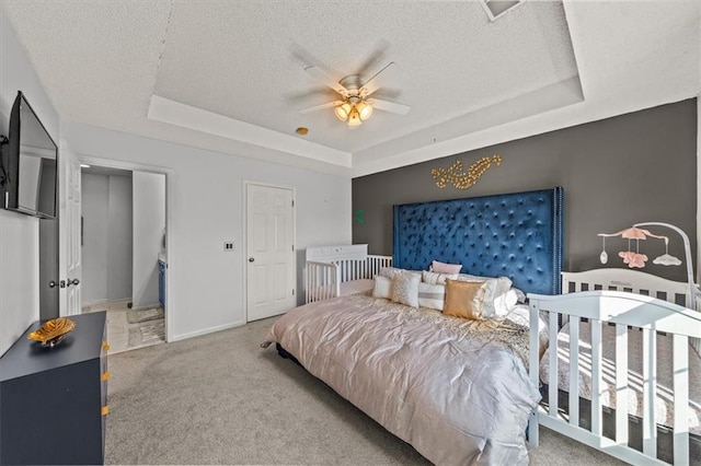 carpeted bedroom featuring ceiling fan, a textured ceiling, a raised ceiling, and baseboards