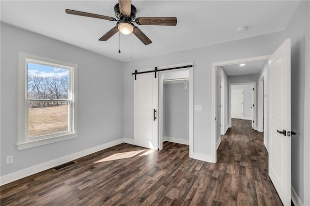 unfurnished bedroom with a barn door, visible vents, baseboards, dark wood-type flooring, and a closet