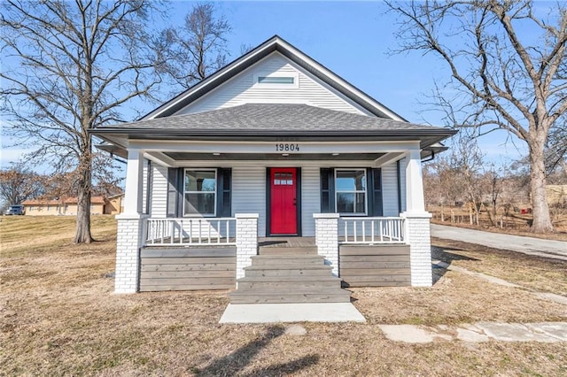 view of front facade with a front yard, covered porch, and roof with shingles