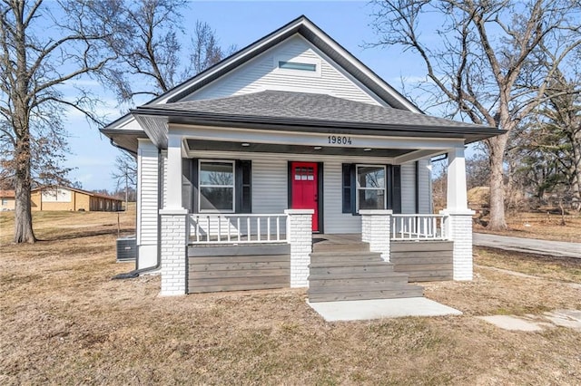 bungalow featuring covered porch, roof with shingles, and a front yard