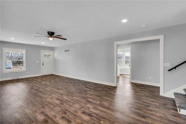 unfurnished living room featuring plenty of natural light, stairs, visible vents, and dark wood finished floors