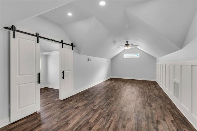 additional living space featuring vaulted ceiling, ceiling fan, a barn door, and dark wood-type flooring