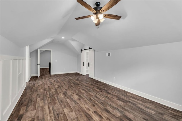 additional living space with dark wood-type flooring, lofted ceiling, baseboards, and a barn door