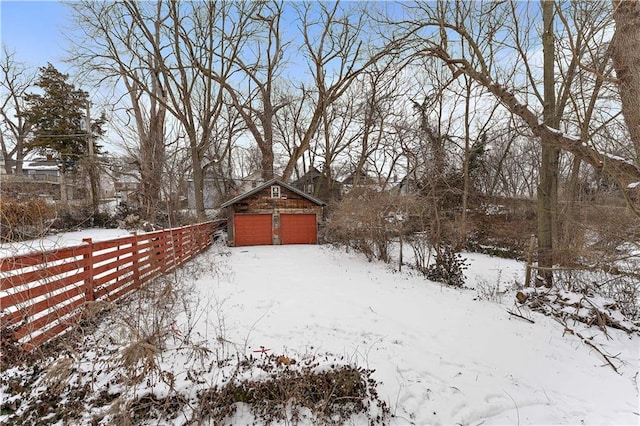 yard layered in snow featuring an outdoor structure, fence, and a detached garage