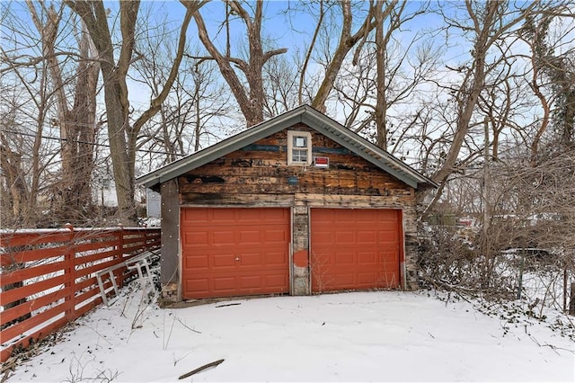 snow covered garage featuring a garage and fence